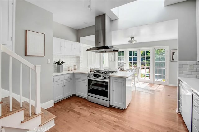 kitchen with kitchen peninsula, island exhaust hood, stainless steel gas range, backsplash, and french doors