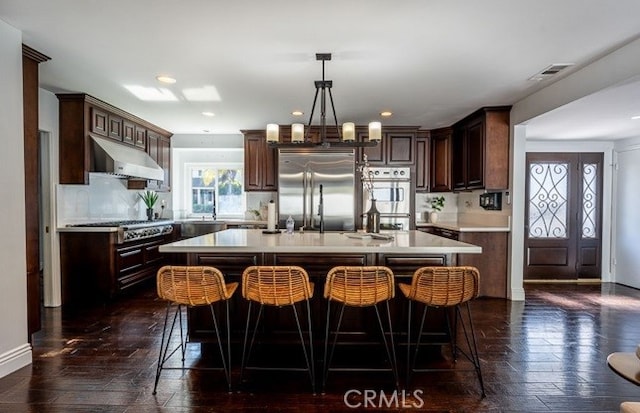 kitchen with stainless steel appliances, dark brown cabinetry, decorative backsplash, a kitchen island, and decorative light fixtures