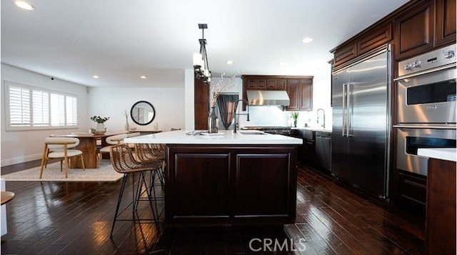 kitchen with pendant lighting, sink, appliances with stainless steel finishes, a kitchen island with sink, and dark brown cabinetry