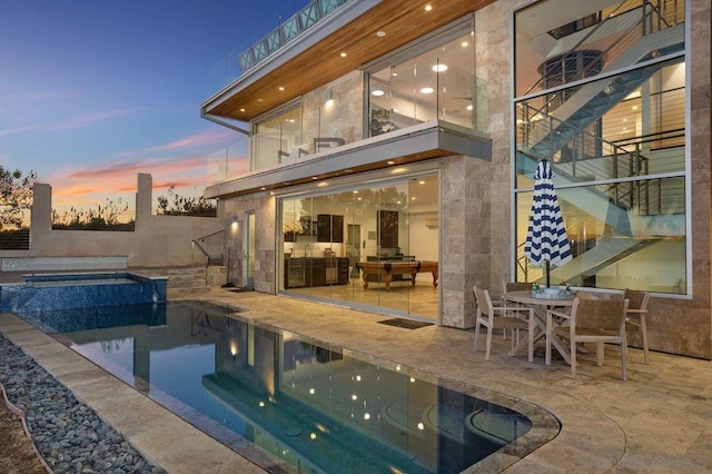 pool at dusk featuring an in ground hot tub and a patio