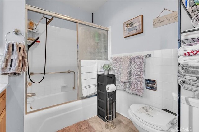 full bathroom with toilet, tile walls, vanity, and shower / bath combination with glass door