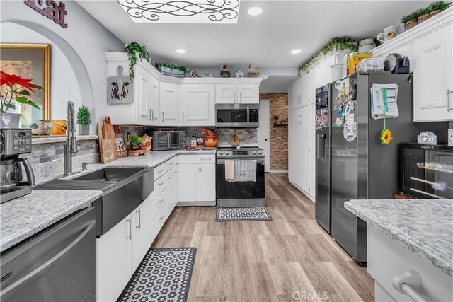 kitchen featuring decorative backsplash, sink, white cabinetry, light wood-type flooring, and stainless steel appliances