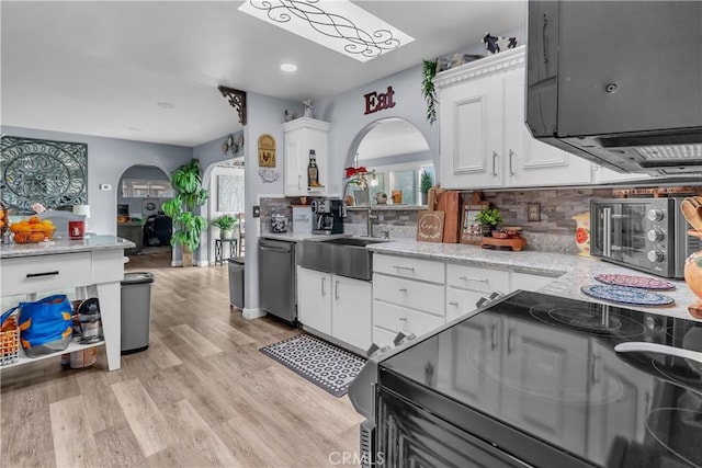 kitchen with white cabinetry, backsplash, light wood-type flooring, dishwasher, and light stone countertops