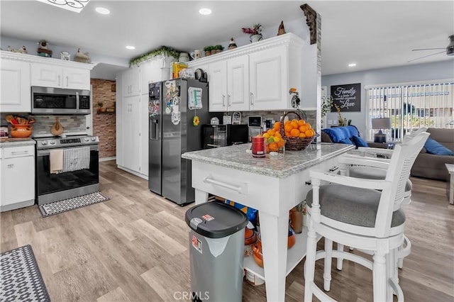 kitchen with light hardwood / wood-style floors, ceiling fan, appliances with stainless steel finishes, decorative backsplash, and white cabinets