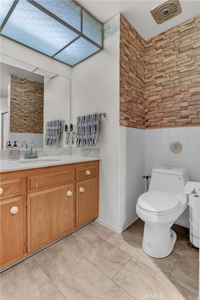 bathroom with tile walls, toilet, and vanity