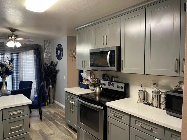 kitchen featuring appliances with stainless steel finishes, gray cabinetry, hardwood / wood-style flooring, ceiling fan, and a textured ceiling