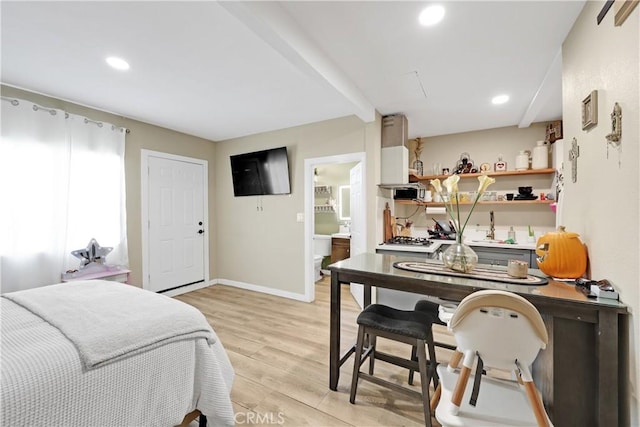 bedroom featuring beamed ceiling, light hardwood / wood-style floors, and ensuite bath