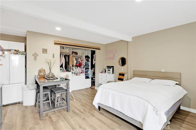 bedroom featuring white fridge, a closet, light hardwood / wood-style flooring, and beamed ceiling