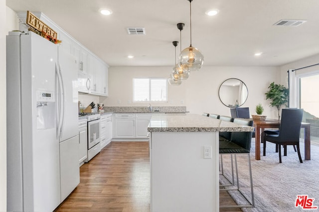 kitchen with white appliances, a kitchen island, white cabinetry, hanging light fixtures, and a breakfast bar area