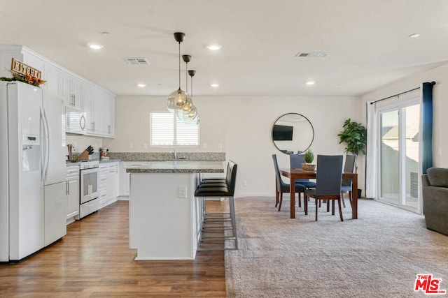 kitchen featuring white appliances, white cabinets, a breakfast bar area, and hanging light fixtures