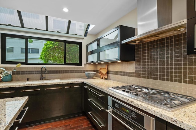 kitchen featuring light stone countertops, appliances with stainless steel finishes, sink, and wall chimney range hood