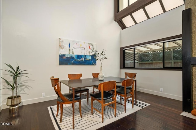 dining space featuring a towering ceiling and dark wood-type flooring