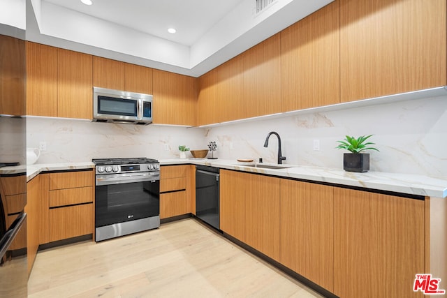 kitchen featuring light stone countertops, appliances with stainless steel finishes, tasteful backsplash, sink, and light wood-type flooring