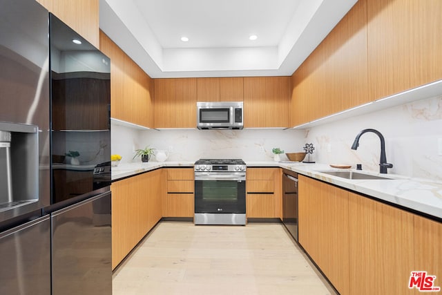 kitchen with black appliances, sink, light stone counters, and light hardwood / wood-style flooring