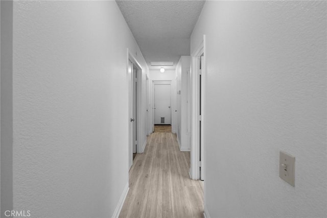 corridor with light wood-type flooring and a textured ceiling