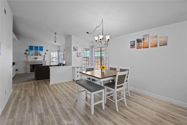 dining space featuring a fireplace, a chandelier, vaulted ceiling, and light hardwood / wood-style flooring