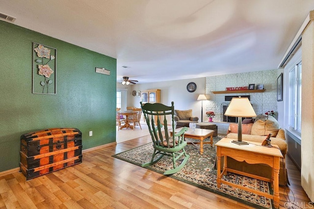 living room with ceiling fan, a large fireplace, and wood-type flooring