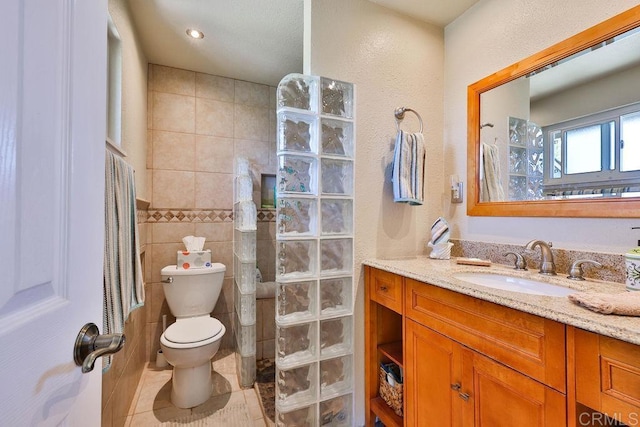 bathroom featuring toilet, tile patterned flooring, tile walls, walk in shower, and vanity