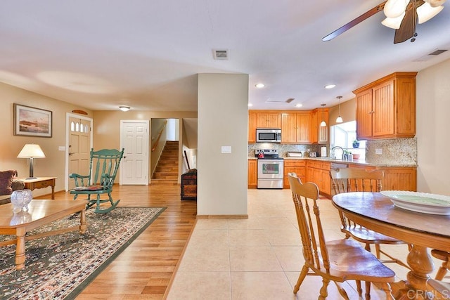 interior space with ceiling fan, appliances with stainless steel finishes, decorative backsplash, pendant lighting, and sink