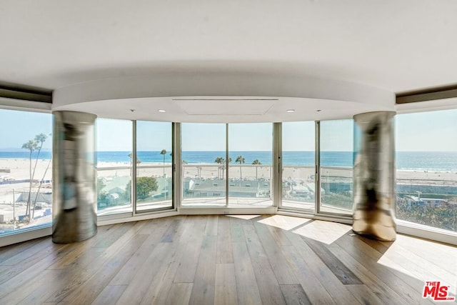 unfurnished room featuring a water view, light wood-type flooring, and a view of the beach