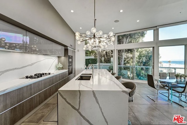 kitchen with an inviting chandelier, a spacious island, gas stovetop, light stone countertops, and sink