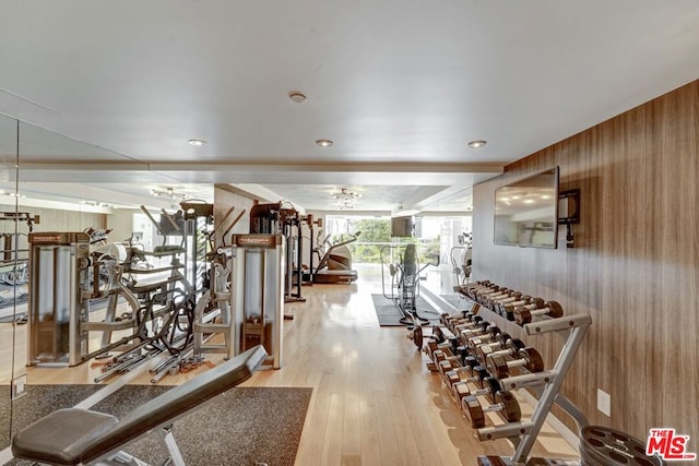 workout area featuring light wood-type flooring, wooden walls, and floor to ceiling windows