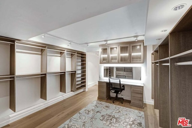 walk in closet with built in desk and light hardwood / wood-style floors