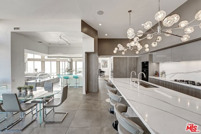 kitchen featuring a notable chandelier, stainless steel gas cooktop, light stone countertops, pendant lighting, and sink