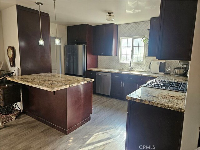 kitchen with backsplash, hanging light fixtures, light wood-type flooring, appliances with stainless steel finishes, and a breakfast bar area