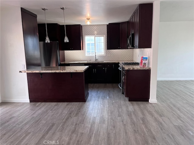 kitchen with sink, a breakfast bar area, decorative light fixtures, light wood-type flooring, and stainless steel appliances