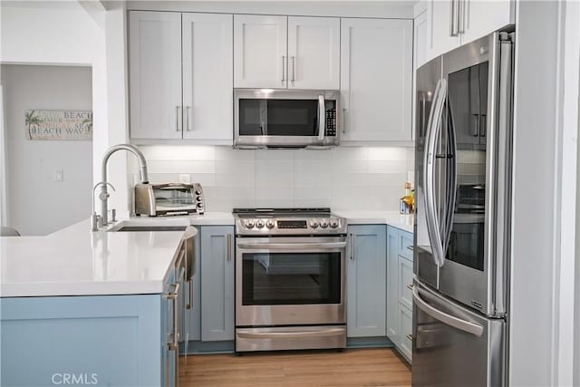 kitchen featuring kitchen peninsula, stainless steel appliances, tasteful backsplash, light hardwood / wood-style flooring, and sink