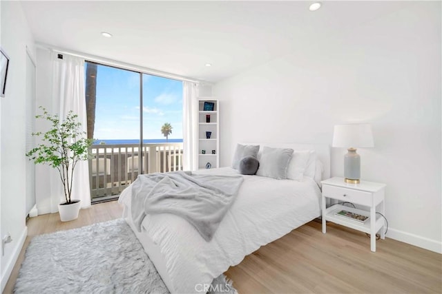 bedroom featuring access to exterior, light hardwood / wood-style floors, a water view, and expansive windows