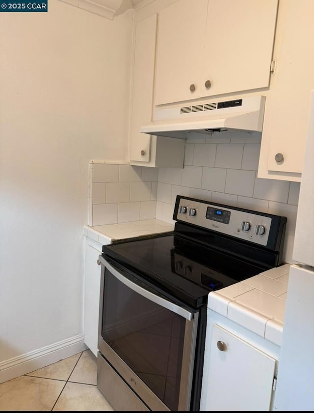 kitchen featuring decorative backsplash, light tile patterned floors, stainless steel electric range oven, tile counters, and white cabinets