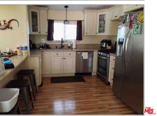 kitchen with stainless steel appliances, sink, hanging light fixtures, cream cabinets, and hardwood / wood-style flooring