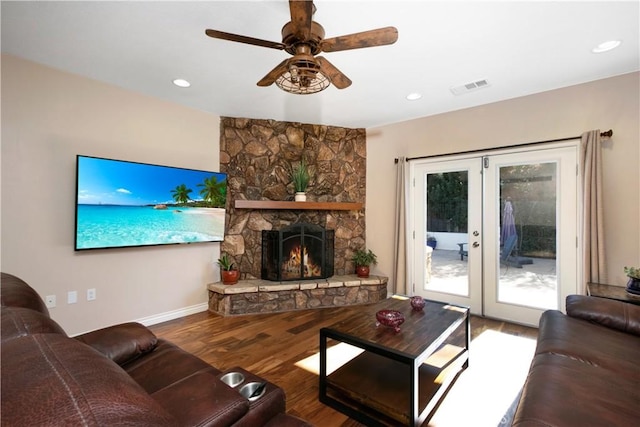 living room featuring ceiling fan, hardwood / wood-style flooring, a healthy amount of sunlight, a stone fireplace, and french doors