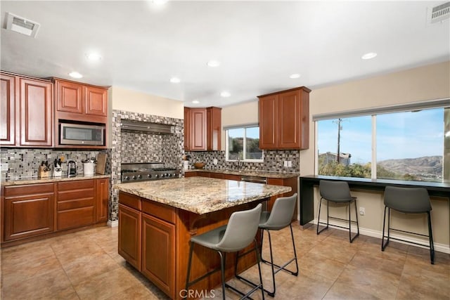 kitchen featuring appliances with stainless steel finishes, a center island, tasteful backsplash, a kitchen breakfast bar, and light stone counters