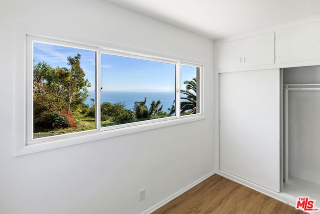 unfurnished bedroom with dark wood-type flooring, a closet, and a water view