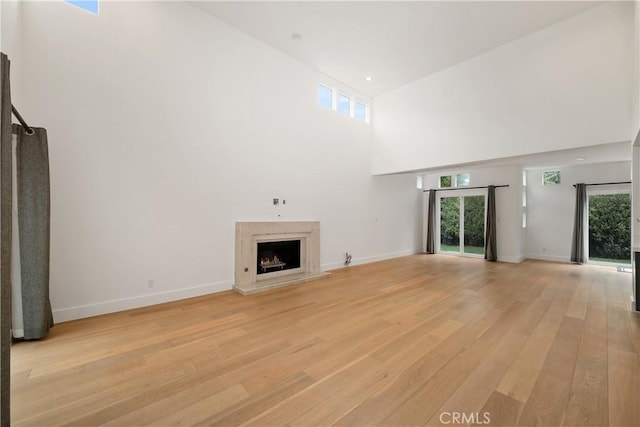 3308 Pacific Ave, Manhattan Beach, CA 90266 - unfurnished living room featuring light wood-style floors, a high ceiling, a lit fireplace, and baseboards