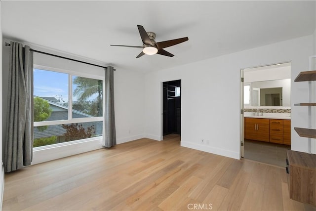 unfurnished bedroom featuring ceiling fan, light hardwood / wood-style floors, ensuite bath, a walk in closet, and a closet