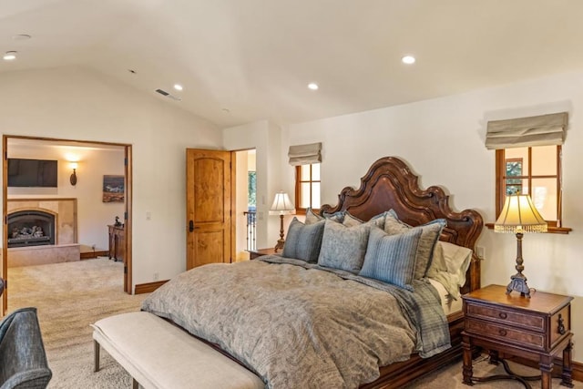 bedroom featuring a tiled fireplace, vaulted ceiling, and light colored carpet