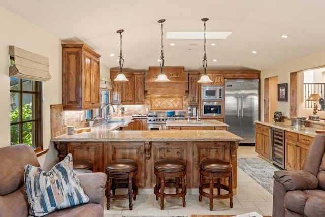 kitchen with a kitchen bar, tasteful backsplash, built in appliances, kitchen peninsula, and beverage cooler