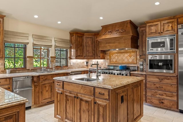 kitchen featuring sink, a kitchen island with sink, stainless steel microwave, light stone countertops, and custom exhaust hood