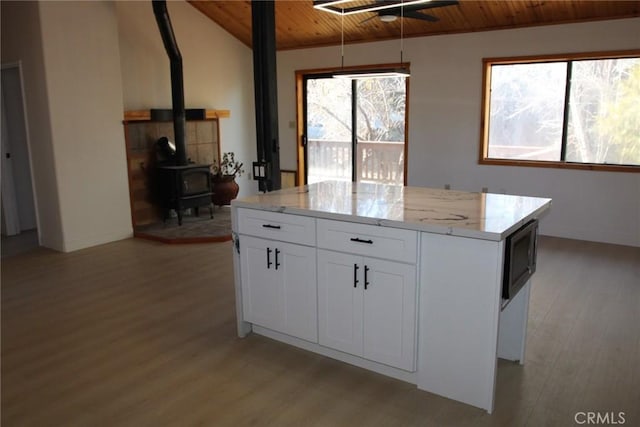 kitchen with a center island, white cabinetry, a wood stove, light stone counters, and wooden ceiling