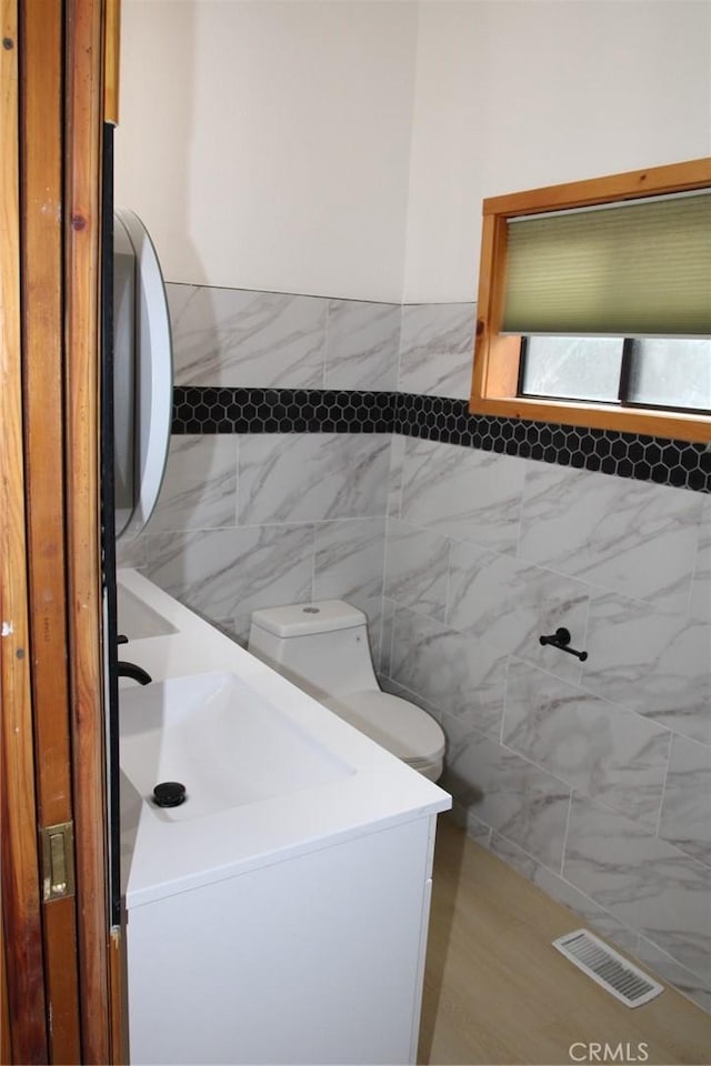 bathroom with toilet, tile walls, and vanity