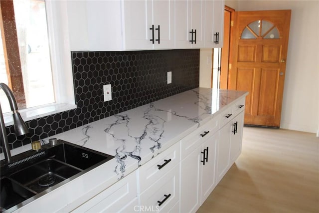 kitchen with white cabinets, decorative backsplash, sink, and light stone counters