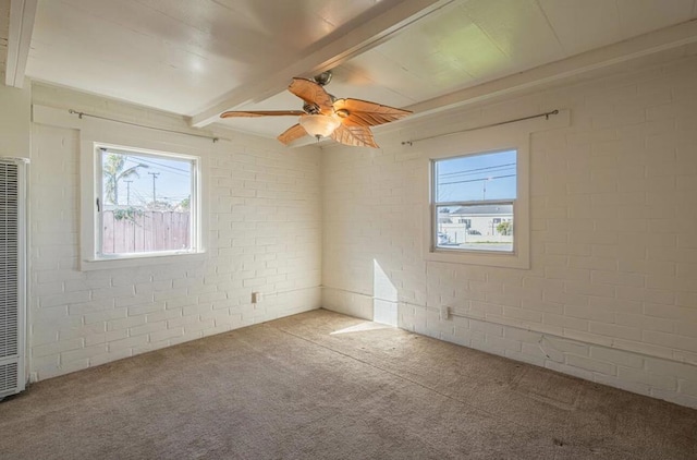 carpeted empty room featuring brick wall, ceiling fan, a wealth of natural light, and beamed ceiling