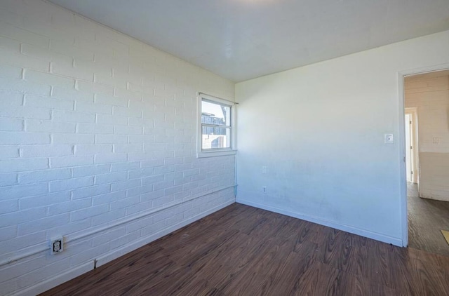 spare room with brick wall and dark hardwood / wood-style floors