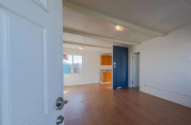 spare room featuring dark wood-type flooring, brick wall, and beam ceiling