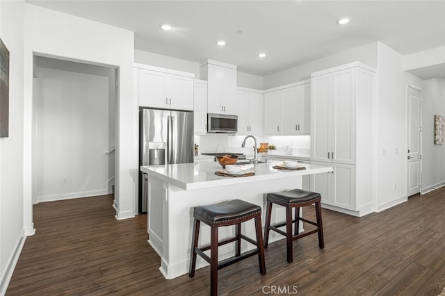 kitchen featuring a kitchen island with sink, stainless steel appliances, a kitchen breakfast bar, and white cabinets