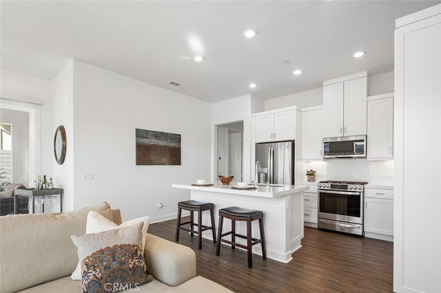 kitchen with a breakfast bar, an island with sink, white cabinets, dark hardwood / wood-style flooring, and stainless steel appliances